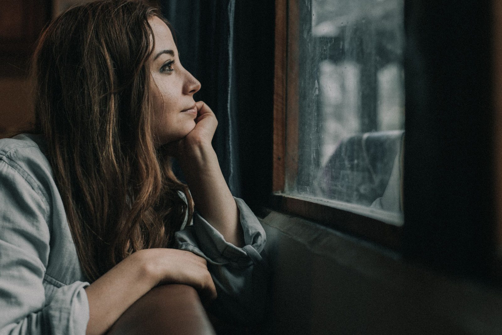 A woman sitting quietly by a window, looking out and thinking
