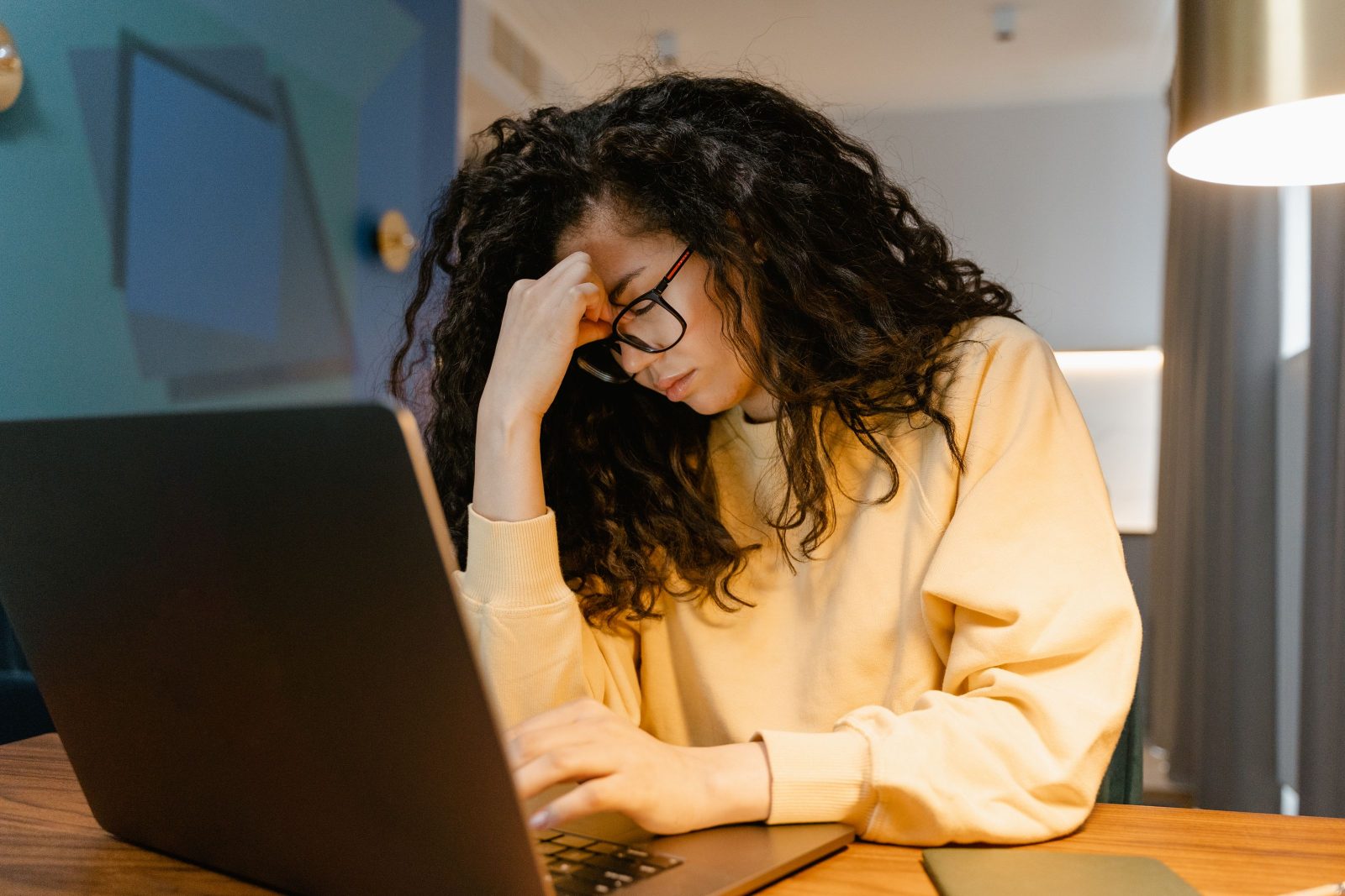 A woman resting her head in her hand at a desk in the evening