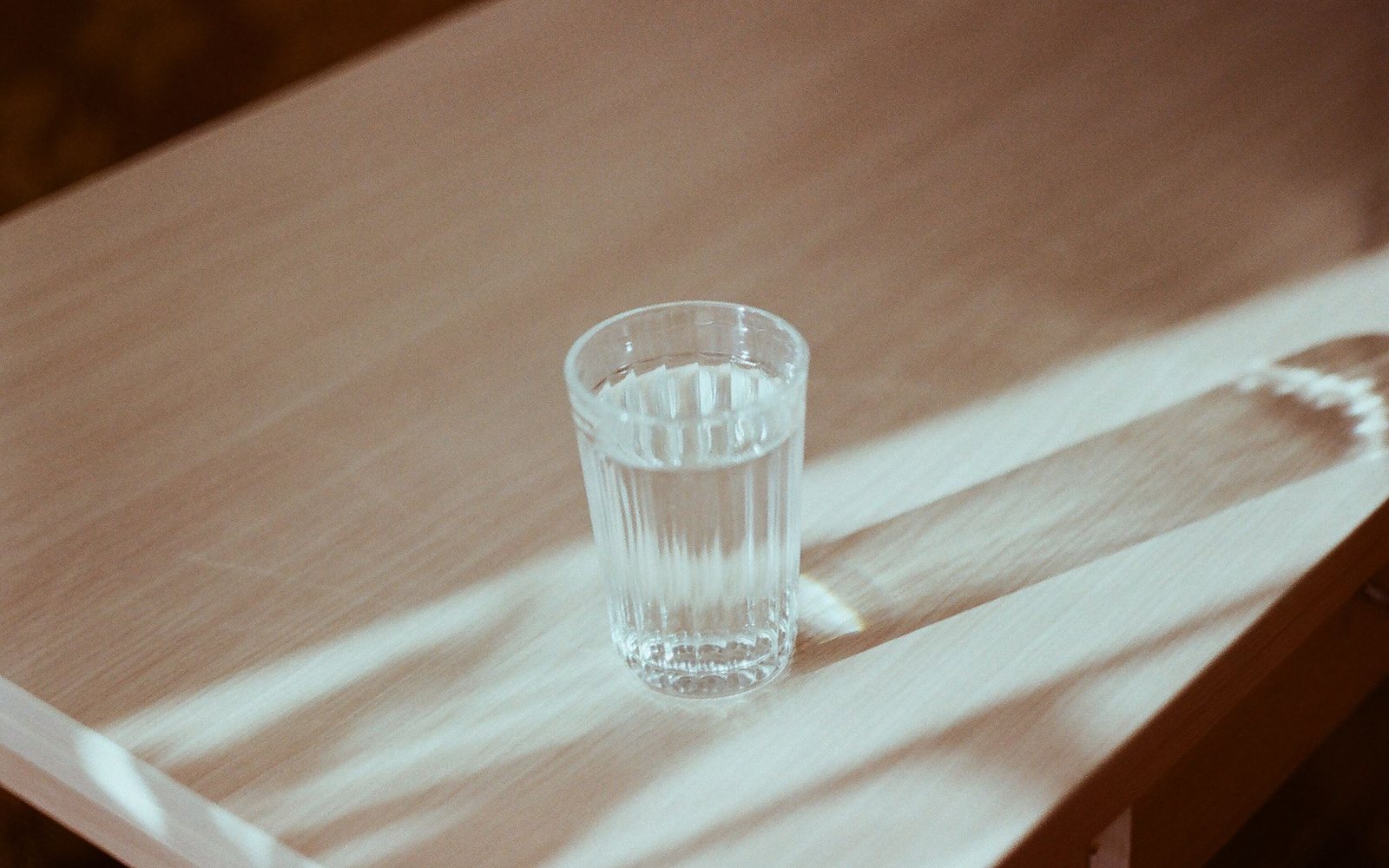 A glass of water on a wooden table in soft morning light