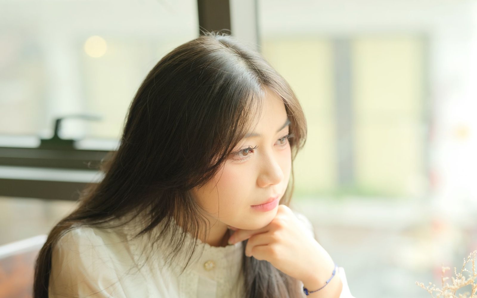 A woman sitting by a window in daylight, thinking