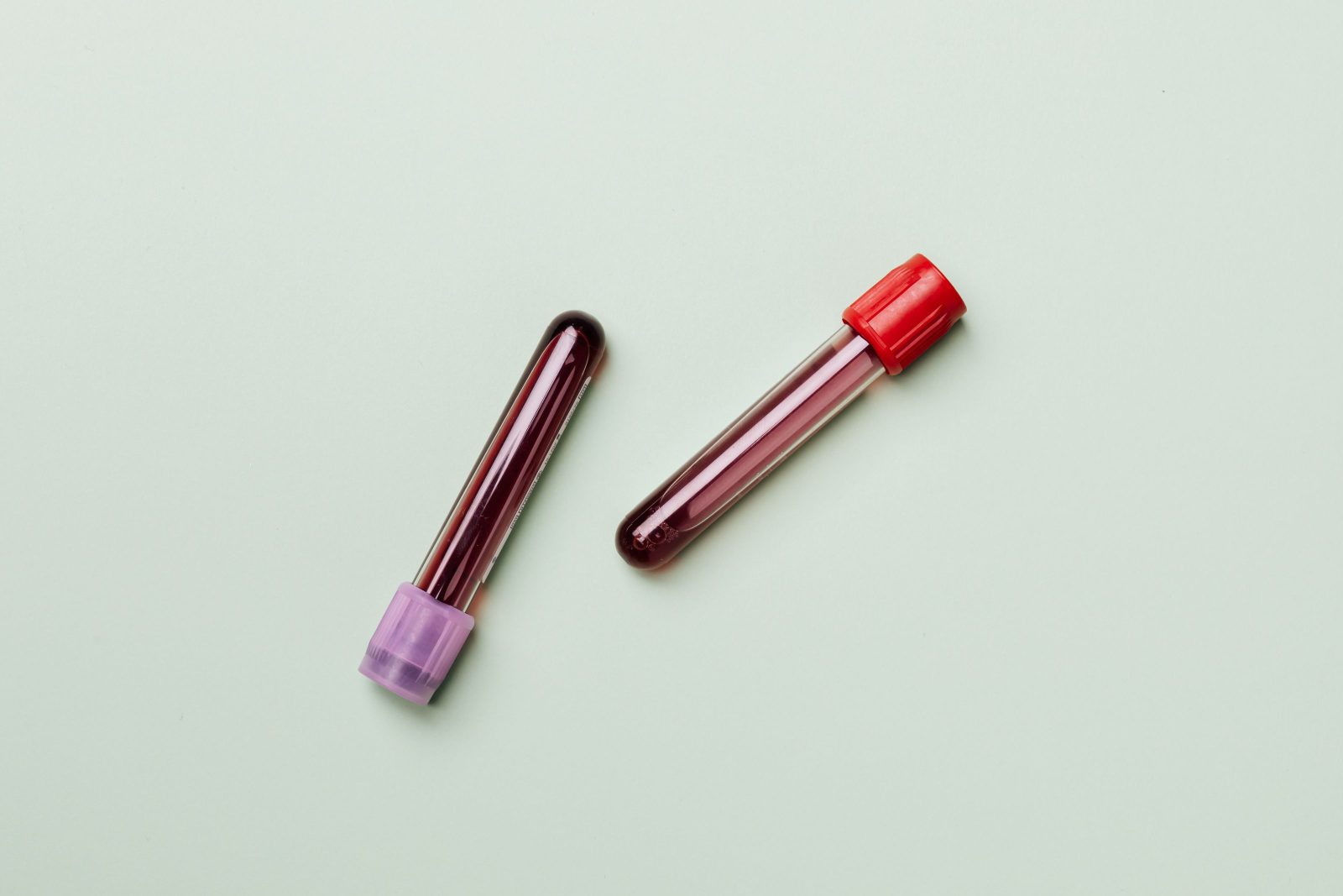 Two blood collection tubes on a pale green surface