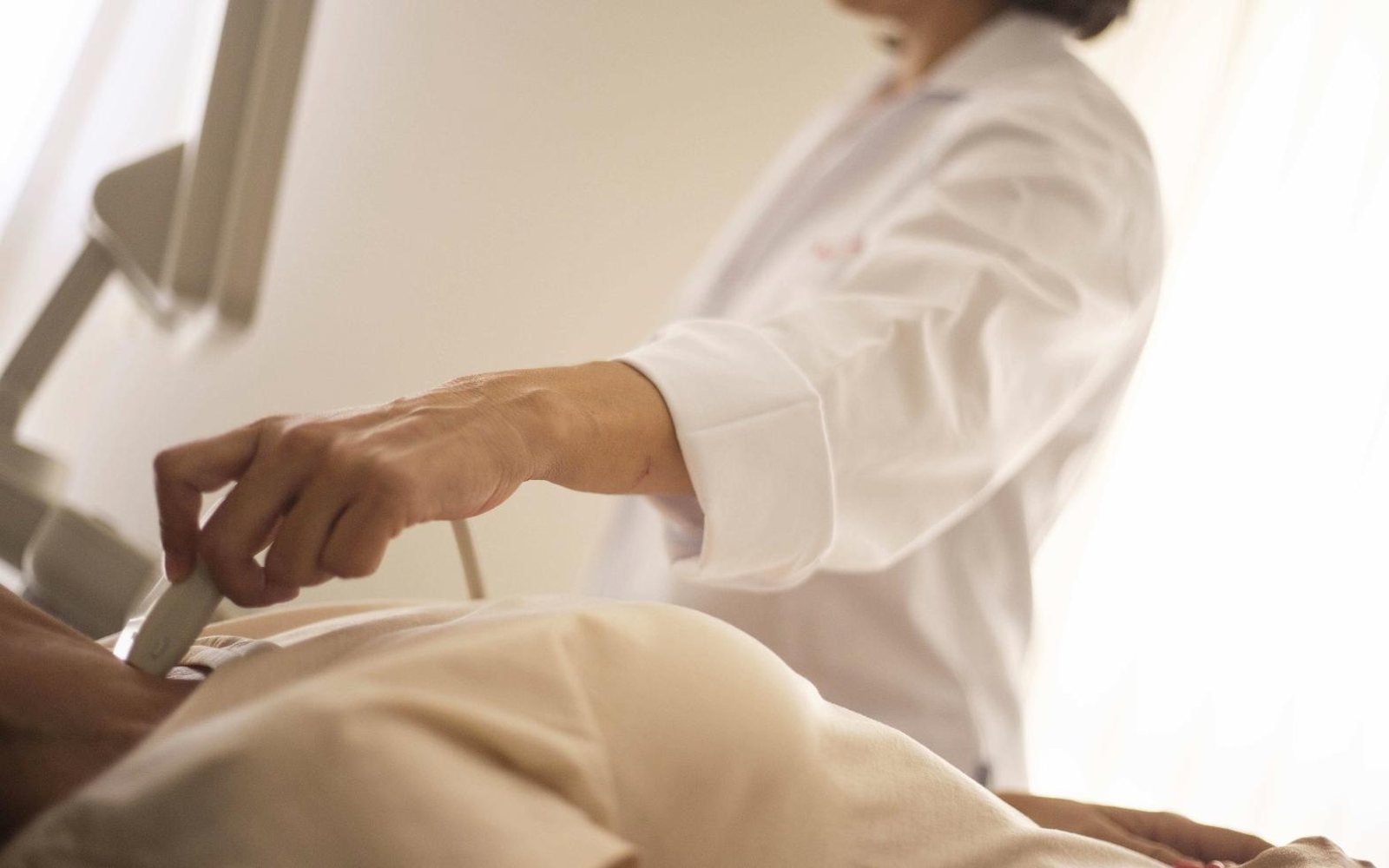 A clinician performing an ultrasound examination on a patient in a bright clinic room