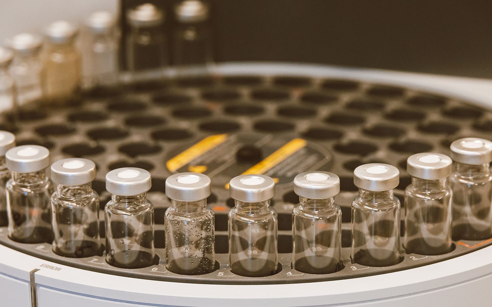 A row of clear glass medication vials with silver caps in a laboratory tray