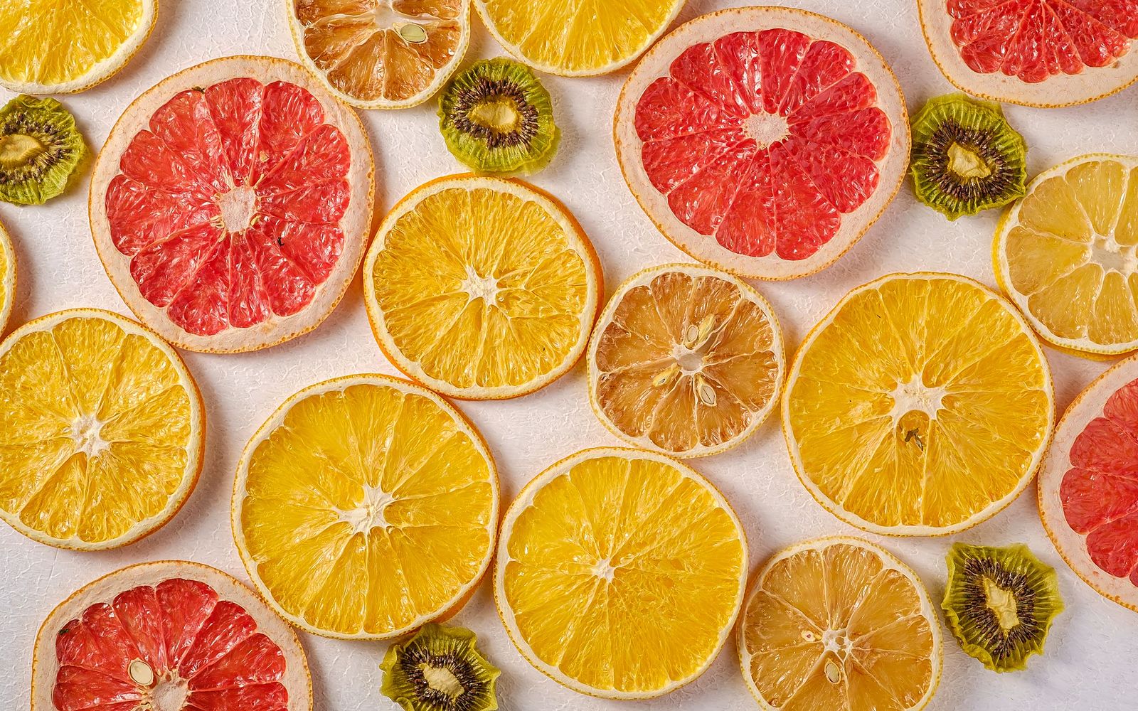 Overhead flat lay of cross-sectioned citrus fruit, orange, grapefruit, lemon and kiwi, on a pale cream background