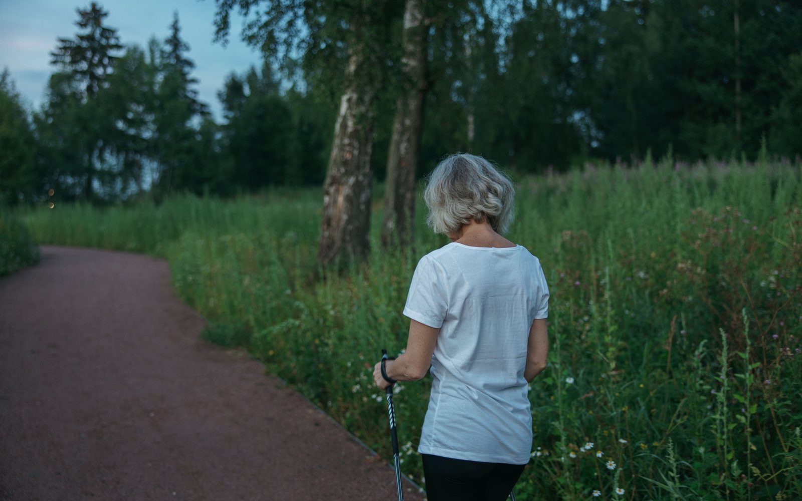 A woman walking on a park path with walking poles, seen from behind